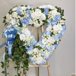 Heart-shaped floral wreath of white and blue flowers on an easel with a blue ribbon