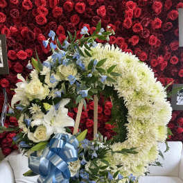 Heart-shaped floral wreath with white flowers, blue accents, and a blue ribbon