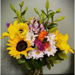 Mixed bouquet of sunflowers, lilies, daisies, and roses in a glass vase