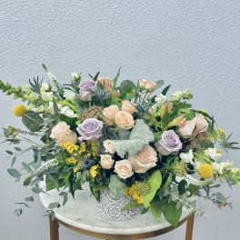 Mixed bouquet of pastel roses and yellow blooms in a decorative white vase
