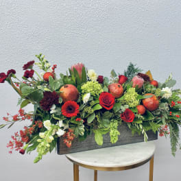 Long rectangular floral arrangement with red and pink blooms and pomegranates