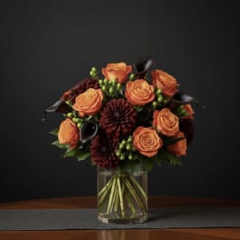 Orange roses and burgundy dahlias in a clear glass vase