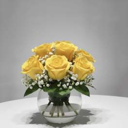 Yellow roses arranged in a clear glass vase with small white filler flowers.