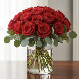 Red roses arranged in a clear glass vase with round greenery