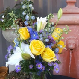 Yellow and white roses with blue and purple flowers in a glass vase