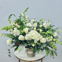 White floral arrangement in a silver vase with green accents