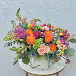 Mixed bouquet of orange, pink, and purple flowers in a white vase