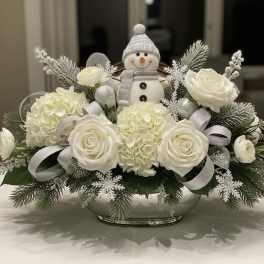 White roses and hydrangeas arranged with a small snowman figurine in a bowl.