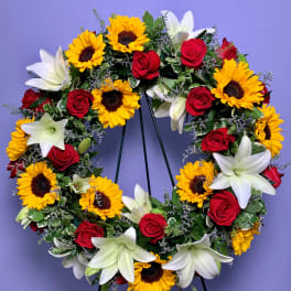 Circular wreath of red roses, white lilies, and yellow sunflowers on a stand