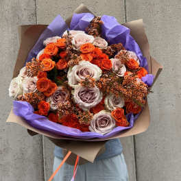 Bouquet of orange and blush roses wrapped in purple paper