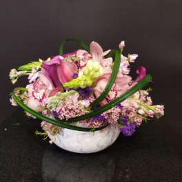 Pink and purple floral arrangement in a white bowl vase