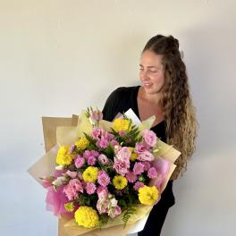 Woman holding a large bouquet of pink and yellow flowers wrapped in paper