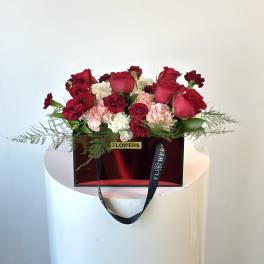 Red roses and pink carnations arranged in a red gift box