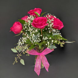 Pink roses in a clear glass vase with baby's breath and a pink ribbon