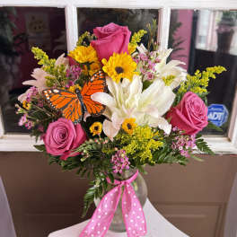 Pink roses and white lilies in a glass vase with a butterfly accent