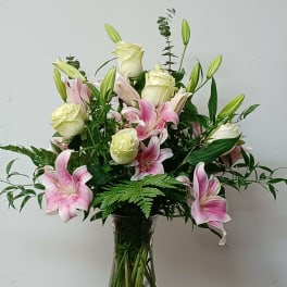 Pink lilies and white roses arranged in a clear glass vase