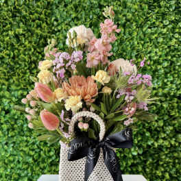 Pastel bouquet of tulips, carnations and mums in a woven cream bag with black ribbon