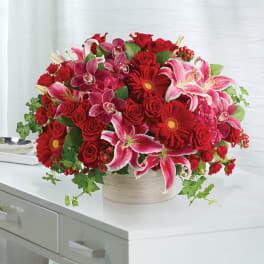 Bouquet of red roses, pink lilies, and red gerbera daisies in a round vase