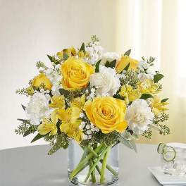 Yellow roses and white flowers arranged in a clear glass vase