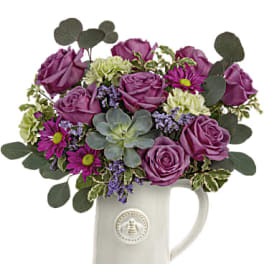 Purple roses and mixed flowers arranged in a white ceramic pitcher