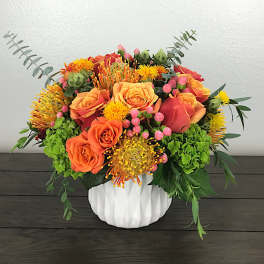 Orange and pink roses in a white vase with green accents