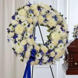 White and blue floral wreath on a stand with a blue ribbon