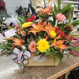 Mixed flower arrangement in a wooden box with orange lilies and yellow mums