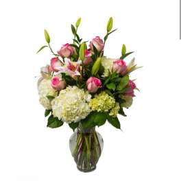 Pink roses and white lilies arranged with hydrangeas in a glass vase