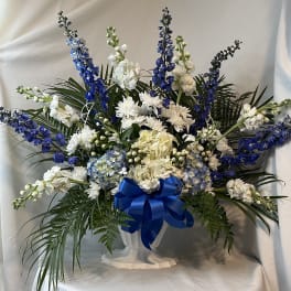 Blue and white floral arrangement in a white pedestal vase with a blue ribbon