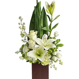 White lilies and roses in a tall wooden vase arrangement
