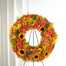 Standing wreath of orange roses, yellow sunflowers, and mixed blooms on a metal easel