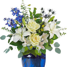 White roses and lilies in a blue glass vase with blue flowers
