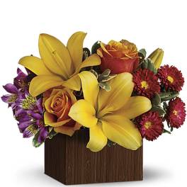 Yellow lilies and orange roses in a wooden cube vase with purple flowers