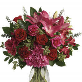 Bouquet of pink lilies, red roses, and hydrangeas in a clear glass vase