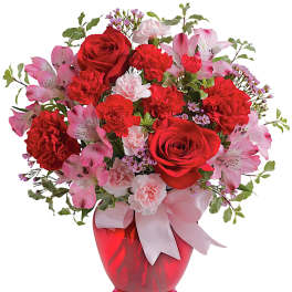 Red roses and pink flowers arranged in a red vase with a ribbon
