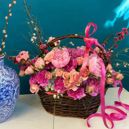 Pink and peach flowers in a wicker basket with a pink ribbon