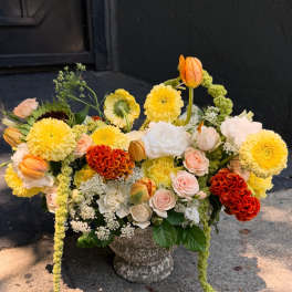 Mixed bouquet in a stone urn with yellow, peach, white, and orange blooms