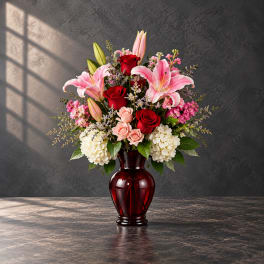 Pink lilies and red roses arranged in a red glass vase