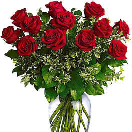 Red roses arranged in a clear glass vase with variegated greenery