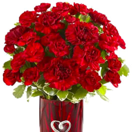 Red carnations in a red glass vase with a heart decoration