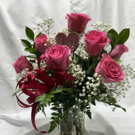 Pink roses in a glass vase with baby's breath and a heart pick