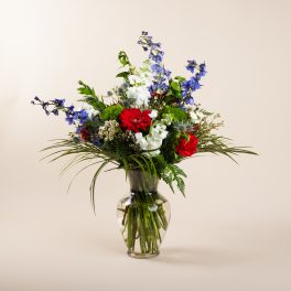 Mixed bouquet of red, white, and blue flowers in a clear glass vase