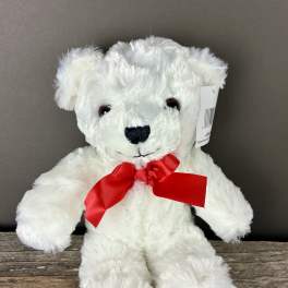 White plush teddy bear with a red bow sitting on a wooden surface