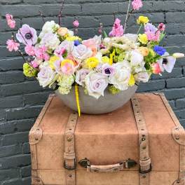 Mixed pastel flower arrangement in a shallow bowl on a vintage suitcase