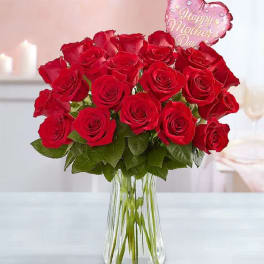 Red roses in a clear glass vase with a pink heart balloon