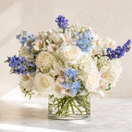 White roses and blue flowers arranged in a clear glass vase