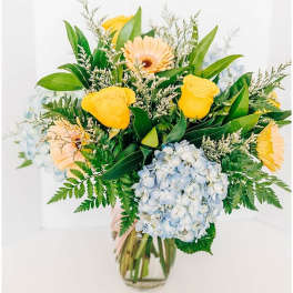Bouquet of yellow roses, gerbera daisies, and blue hydrangea in a glass vase