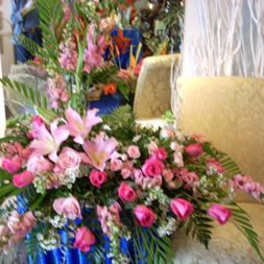 Large pink floral arrangement with lilies and roses on a blue drape