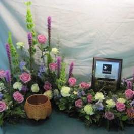 Floral arrangement with pink roses and tall purple spikes around a framed plaque