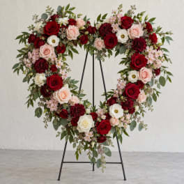 Heart-shaped floral wreath on a black stand with red, pink, and white roses